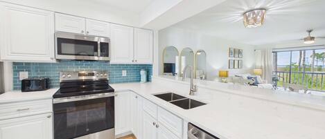 A modern kitchen with stainless steel appliances, a large window, and a balcony with a view.