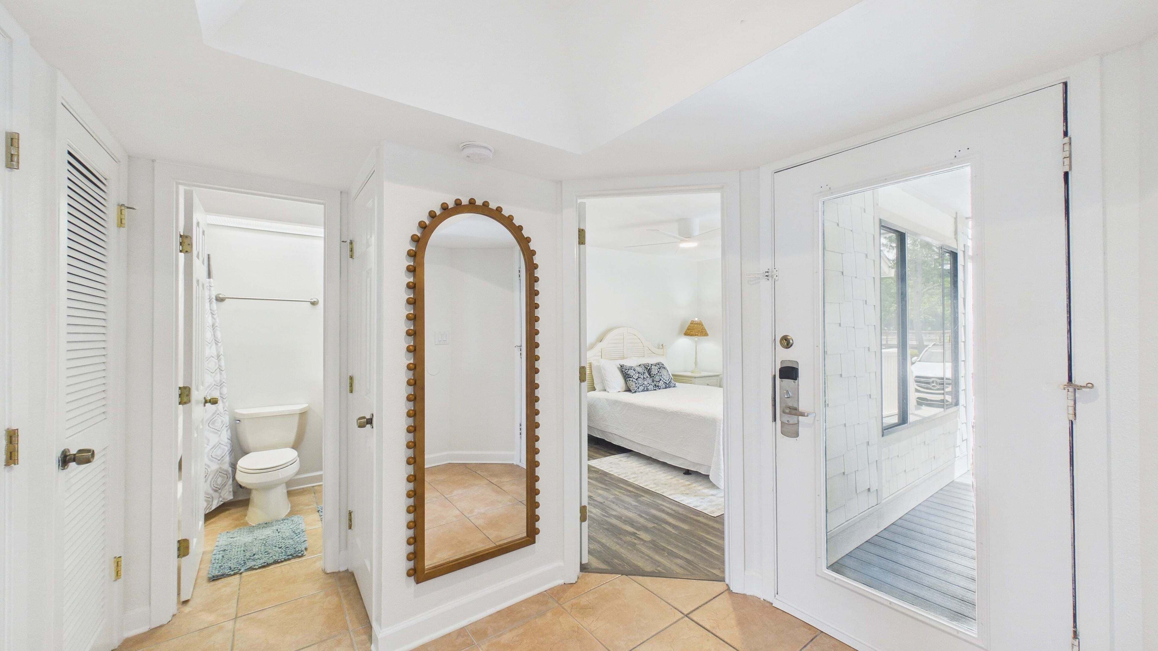 A hotel room with a bathroom, a large mirror, a bed, and a view of the outside.