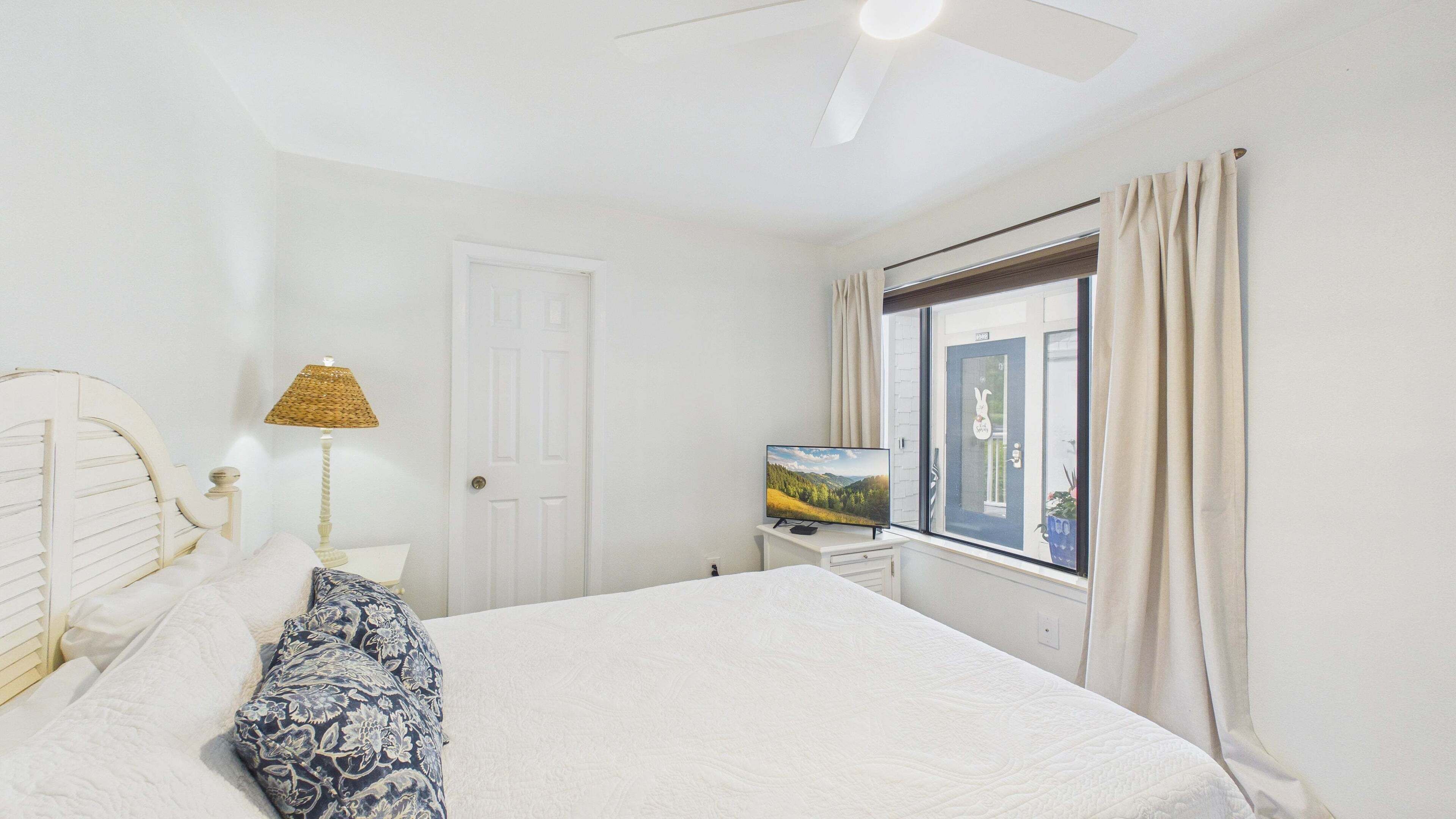 Un dormitorio con cama, televisor, lámpara y ventana con cortinas.