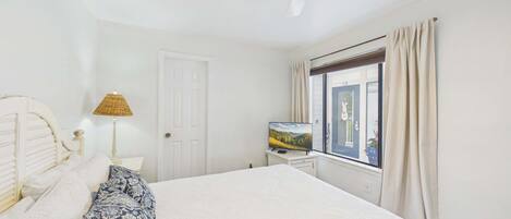 Un dormitorio con cama, televisor, lámpara y ventana con cortinas.