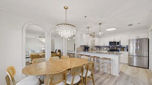 A modern kitchen with white cabinetry, stainless steel appliances, and a wooden dining table with wicker chairs. - Sandy Spires 403-Gulf Views-Sleeps 8 (Seagrove Beach)