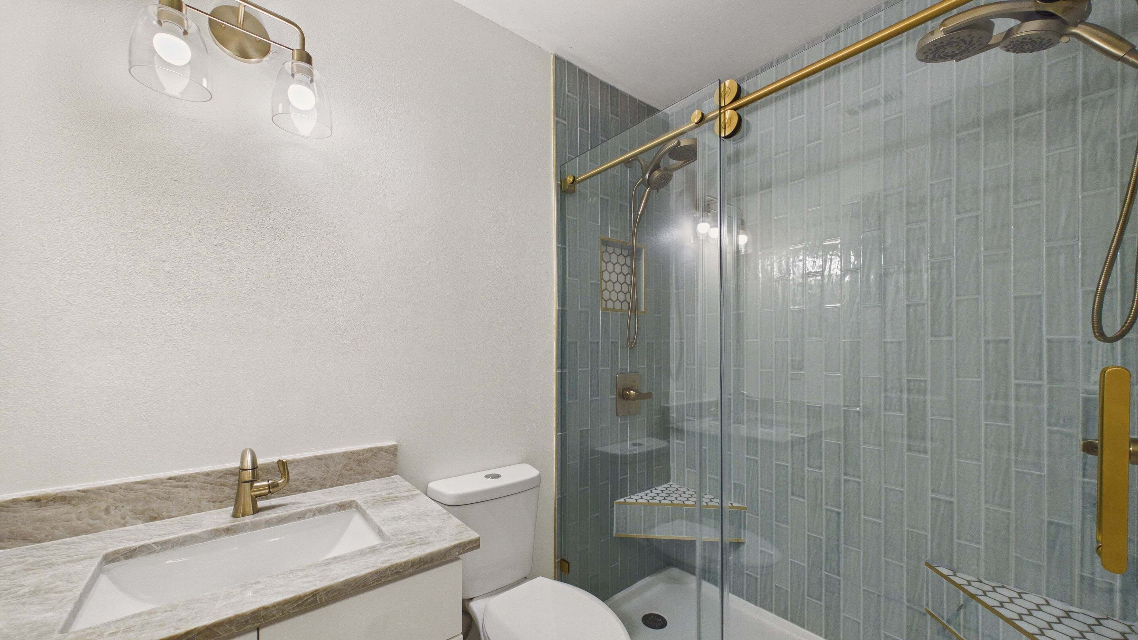 Un baño con ducha de vidrio, lavamanos de mármol y un inodoro.