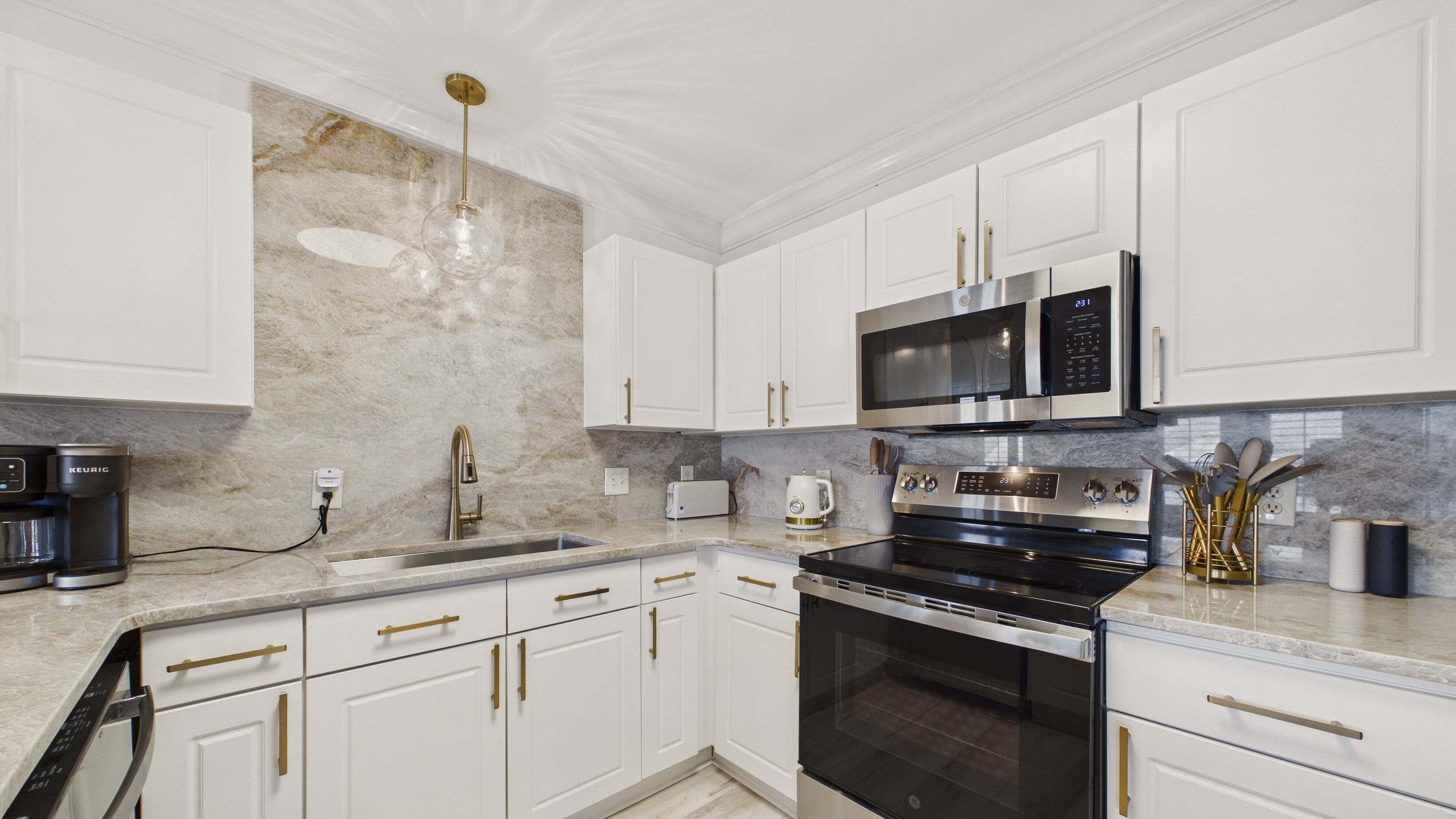 A modern kitchen with white cabinets, a stainless steel microwave, a coffee maker, and a gas stove.