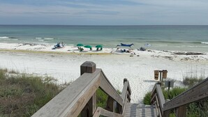 A beach with a wooden boardwalk leading to the shore, green umbrellas, and beach chairs. - Sandy Spires 403-Gulf Views-Sleeps 8 (Seagrove Beach)