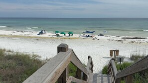 Une plage avec une promenade en bois menant au rivage, des parasols verts et des chaises de plage.