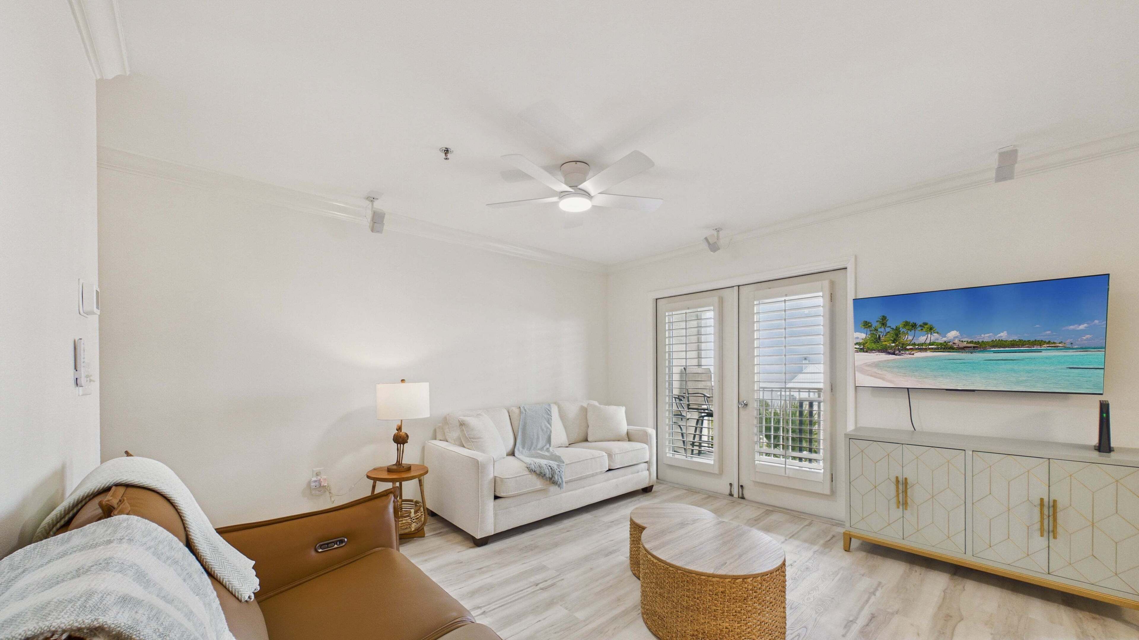 A hotel room with a bed, a sofa, a TV, a ceiling fan, and a view of the beach.