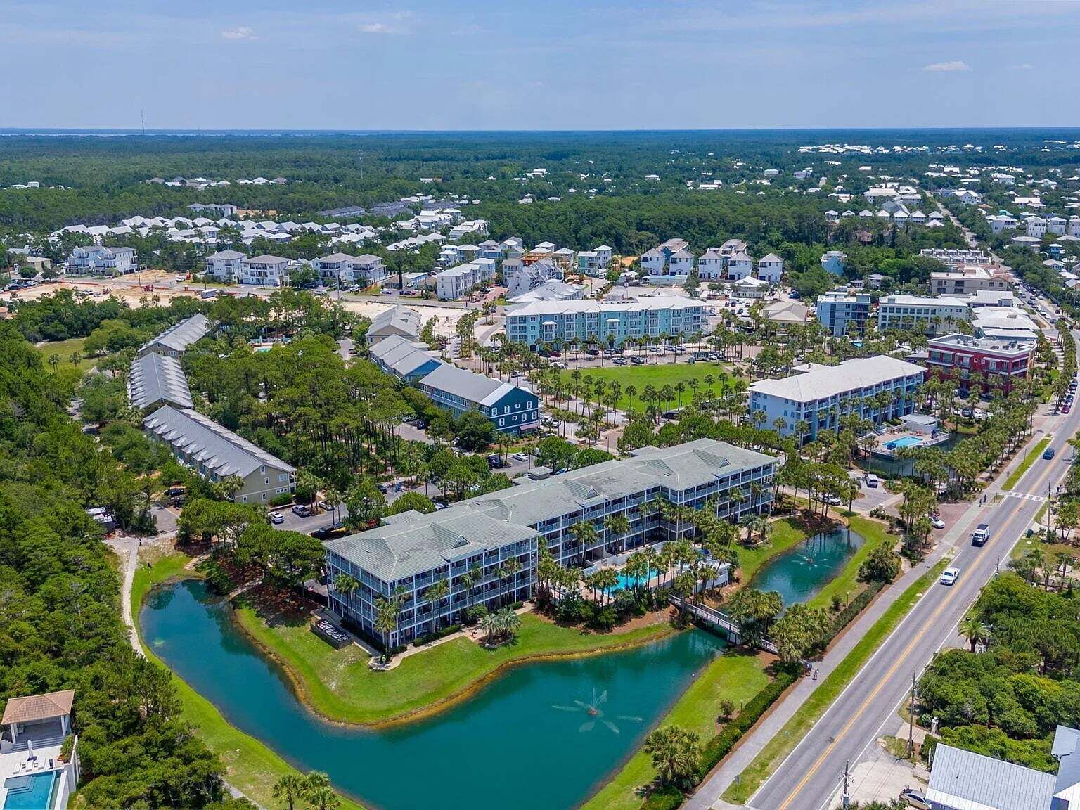 An aerial view of a residential area with a large building complex, a lake, and surrounding greenery.