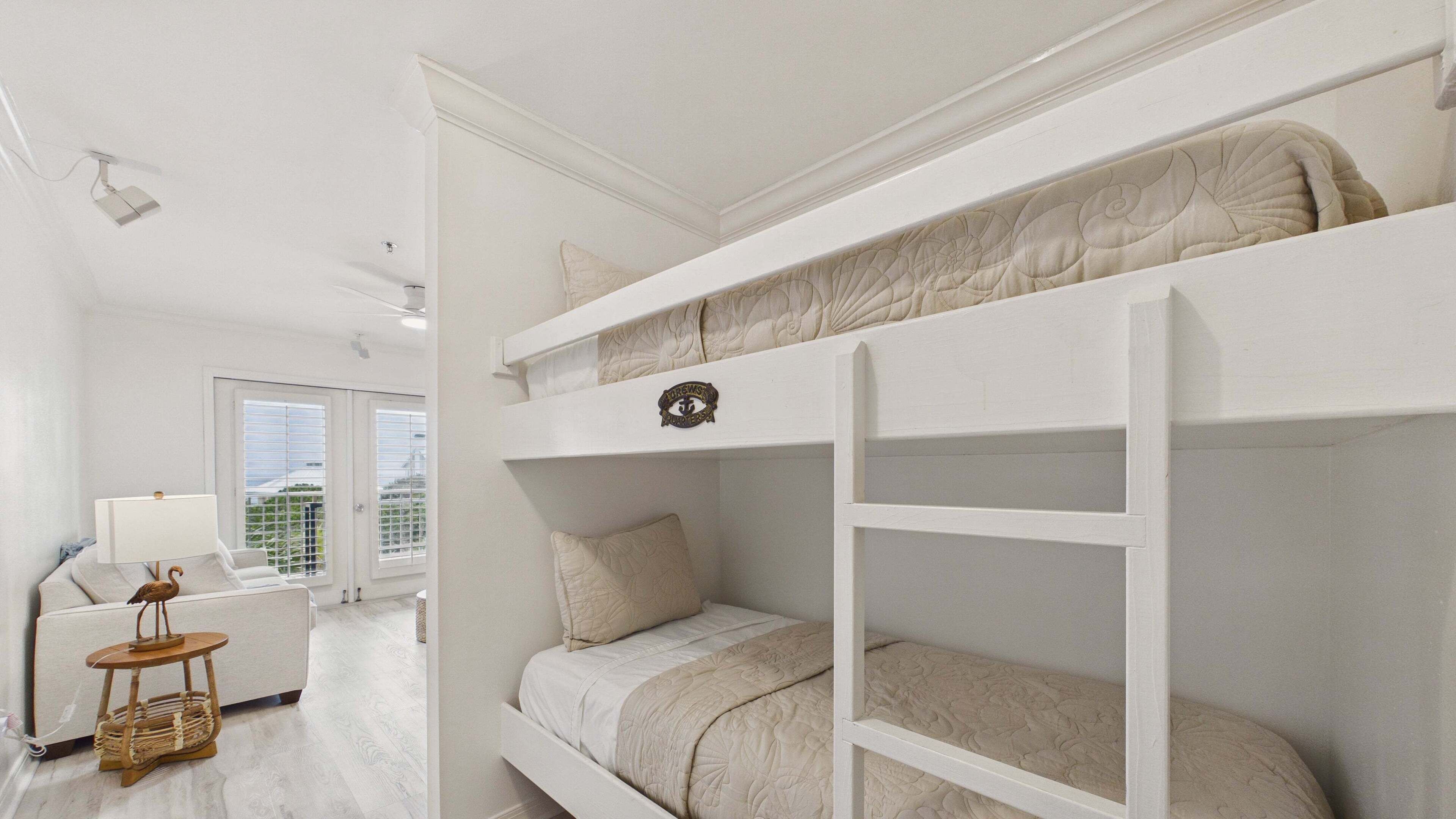 Een slaapkamer met een stapelbed, bureau, lamp en raam.