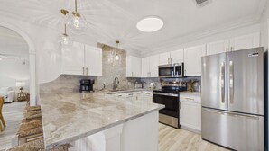 A modern kitchen with white cabinetry, a stainless steel refrigerator, a built-in oven, a microwave, and a coffee maker. - Sandy Spires 403-Gulf Views-Sleeps 8 (Seagrove Beach)