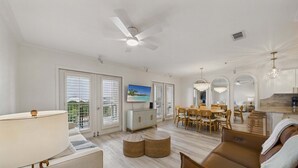 A spacious living area with a ceiling fan, a dining table with chairs, a TV mounted on the wall, and a view through the sliding doors. - Sandy Spires 403-Gulf Views-Sleeps 8 (Seagrove Beach)