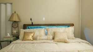 Una cama bien hecha con cabecera, una mesita de noche con lámpara y otro pequeño mueble con una caja de pañuelos.