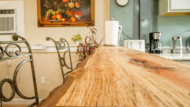 Una cocina con una mesa de madera, una silla de metal, un cuadro, un reloj y un refrigerador.