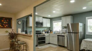 Una cocina moderna con electrodomésticos de acero inoxidable, una zona de comedor con un taburete de bar y un cuadro en la pared.