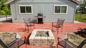 Un patio con dos sillas de metal, una parrilla y un pozo para fuego.