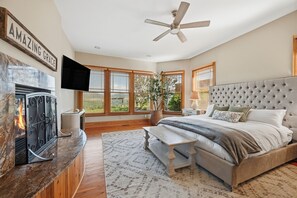 Ein Schlafzimmer mit Bett, Deckenventilator, Kamin und großen Fenstern.