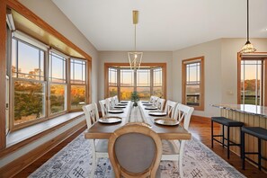 Ein Esszimmer mit einem langen Tisch, gedeckt für sechs Personen, großen Fenstern und Blick auf Bäume.