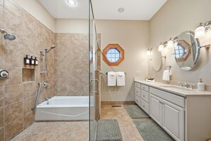 A modern bathroom with a glass-enclosed shower, a bathtub, a vanity with a mirror, and a window above the sink. - Spacious Estate that sleeps 16 near Watauga Lake - walk to Villa Nove Vineyards! (Butler)