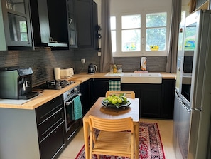 Een kleine keuken met donkere kastjes, een gasfornuis, een koffiezetapparaat, een spoelbak en een eethoek met een tafel en stoelen.