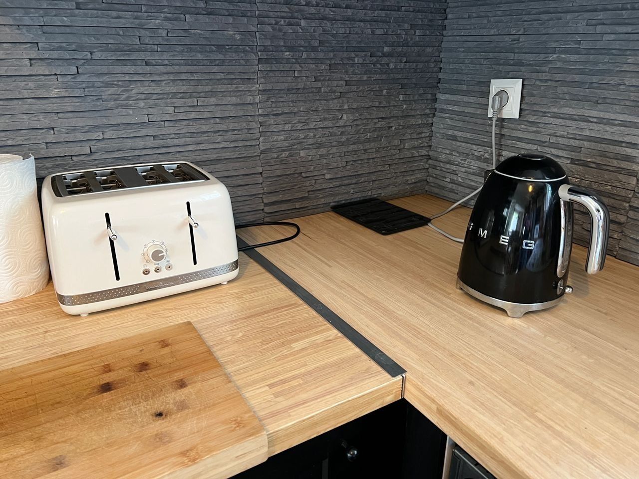 Une cuisine équipée d’un grille-pain, d’une bouilloire et d’une planche à découper en bois posée sur un plan de travail.