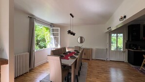 Uma área de refeições com uma mesa comprida posta para quatro pessoas, uma cozinha com micro-ondas e vista para o exterior.