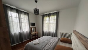 Um quarto com cama, escrivaninha, cadeira, radiador e cortinas.