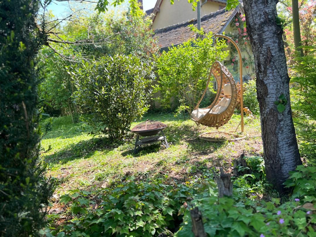 Un jardin avec une balançoire, une petite brouette et un arbre.