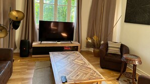 Uma sala de estar com televisão, piso de madeira, sofá, mesa de centro e janela com cortinas.