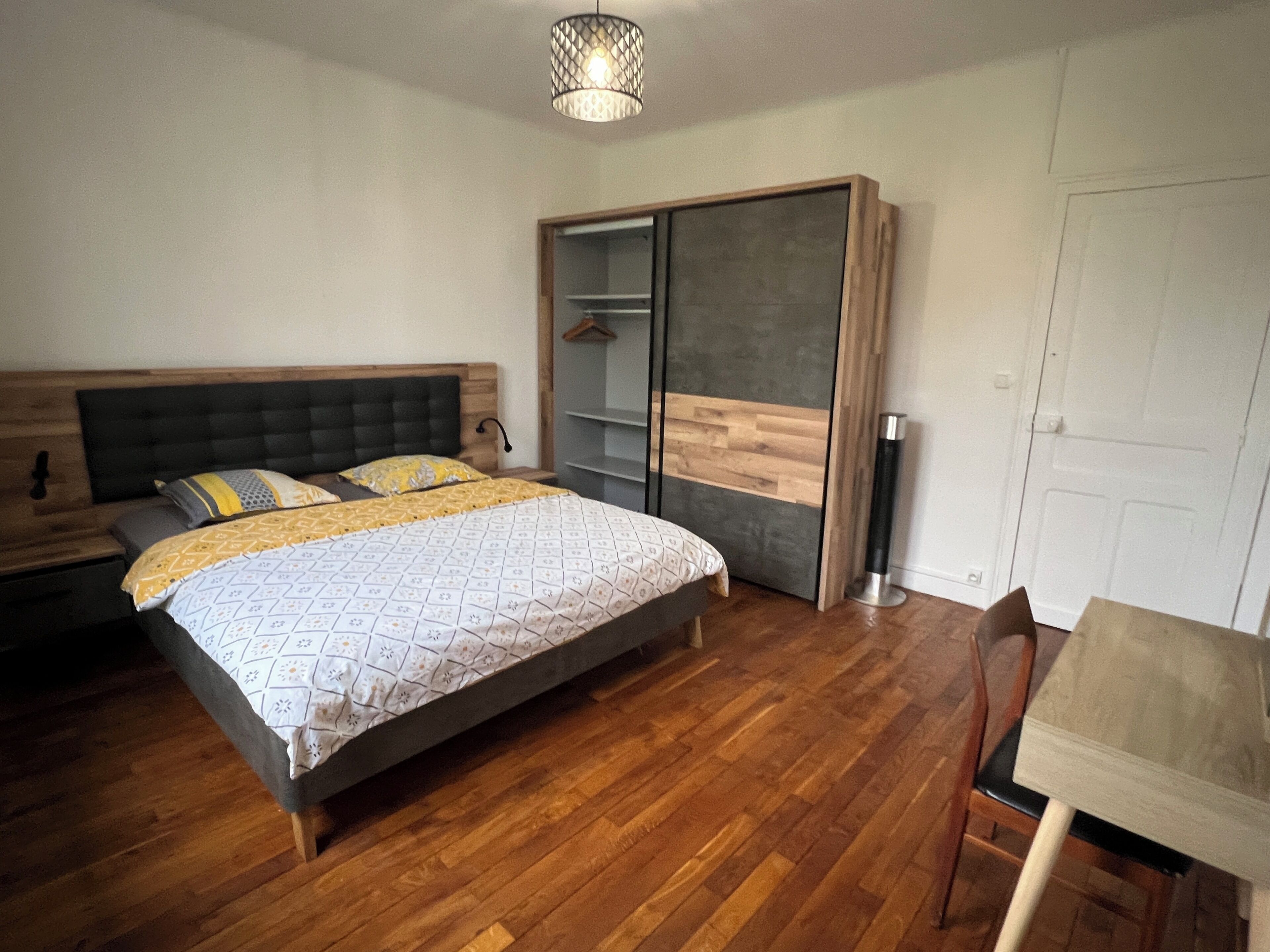 Ein Schlafzimmer mit Bett, Holzboden, Kleiderschrank, Schreibtisch und einer Pendelleuchte.