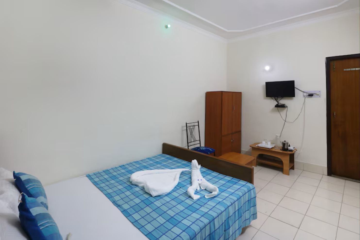 Una habitación de hotel con cama, armario, televisor y una mesita con lámpara.