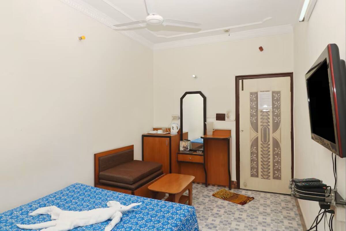 A hotel room with a bed, a desk, a chair, a television, and a wardrobe.