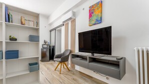 A modern living room with a TV, bookshelf, and a chair. - New Studio at the Gateway to the Alpilles with Pool and Large Garden (Noves)