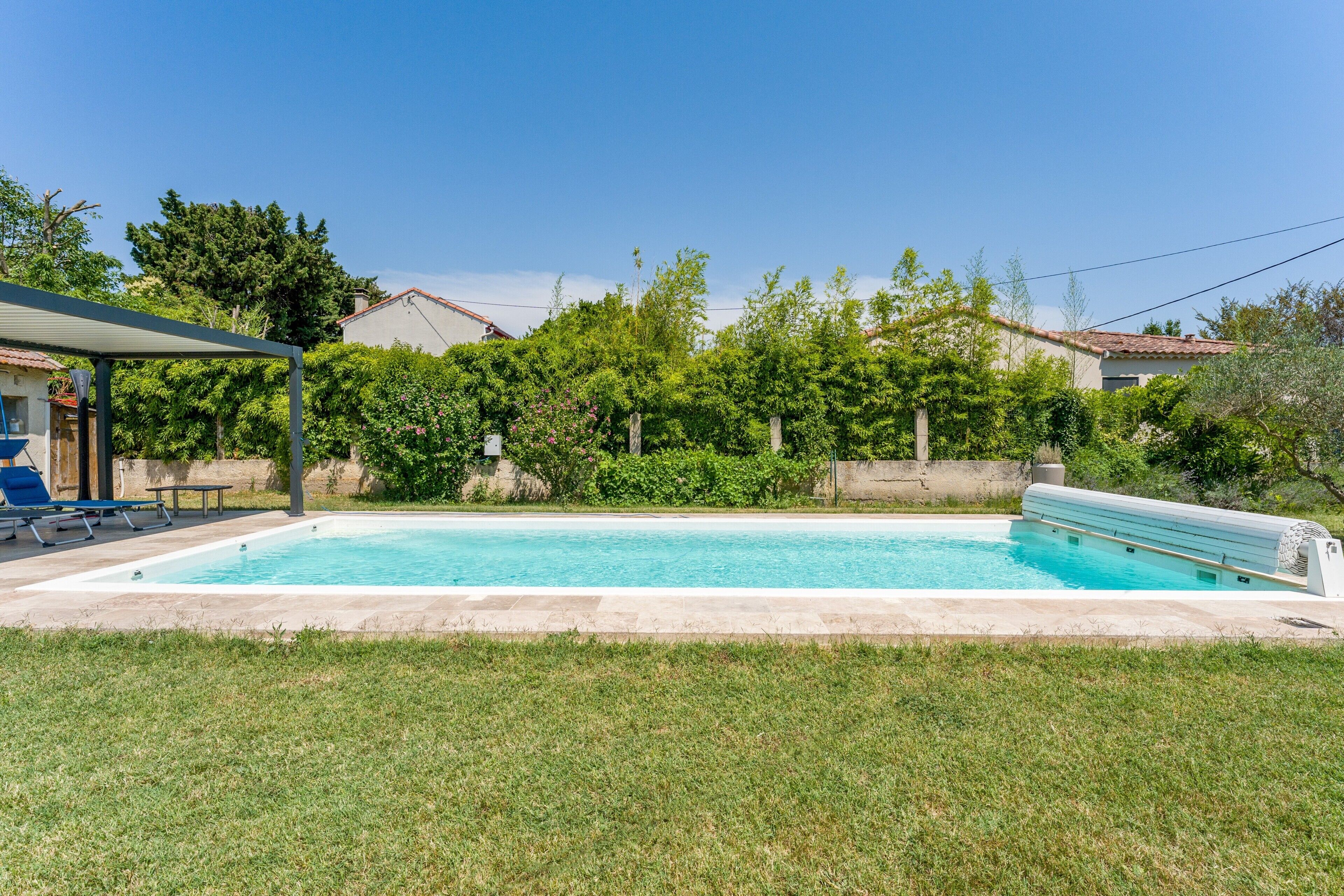 A rectangular swimming pool with a tiled deck, surrounded by a grassy lawn and trees.