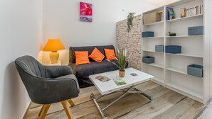 A living room with a sofa, armchair, coffee table, bookshelf, and a lamp. - New Studio at the Gateway to the Alpilles with Pool and Large Garden (Noves)