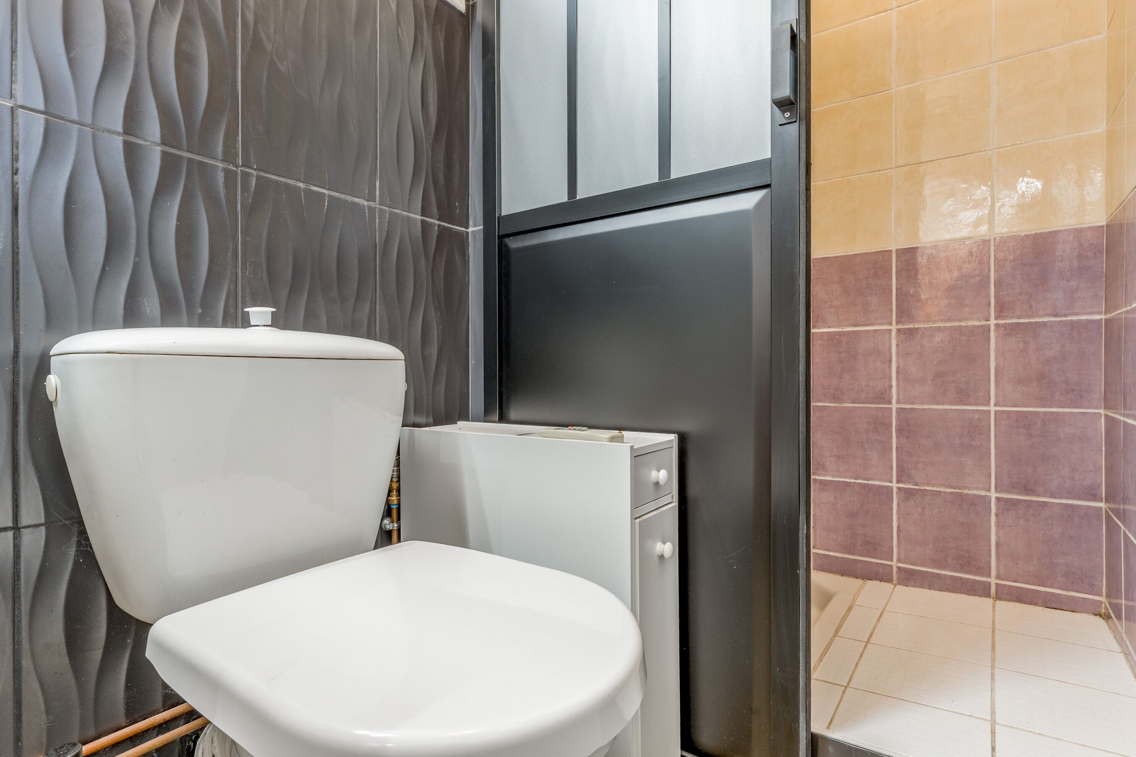 Un baño con inodoro, un armario y pared con azulejos.