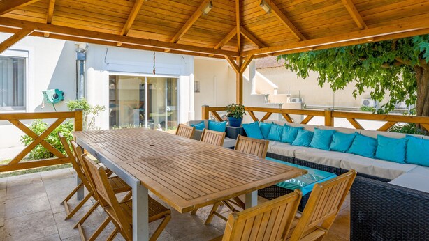 An outdoor patio with a wooden table and chairs, a sofa with cushions, and a pergola overhead. - New Studio at the Gateway to the Alpilles with Pool and Large Garden (Noves)