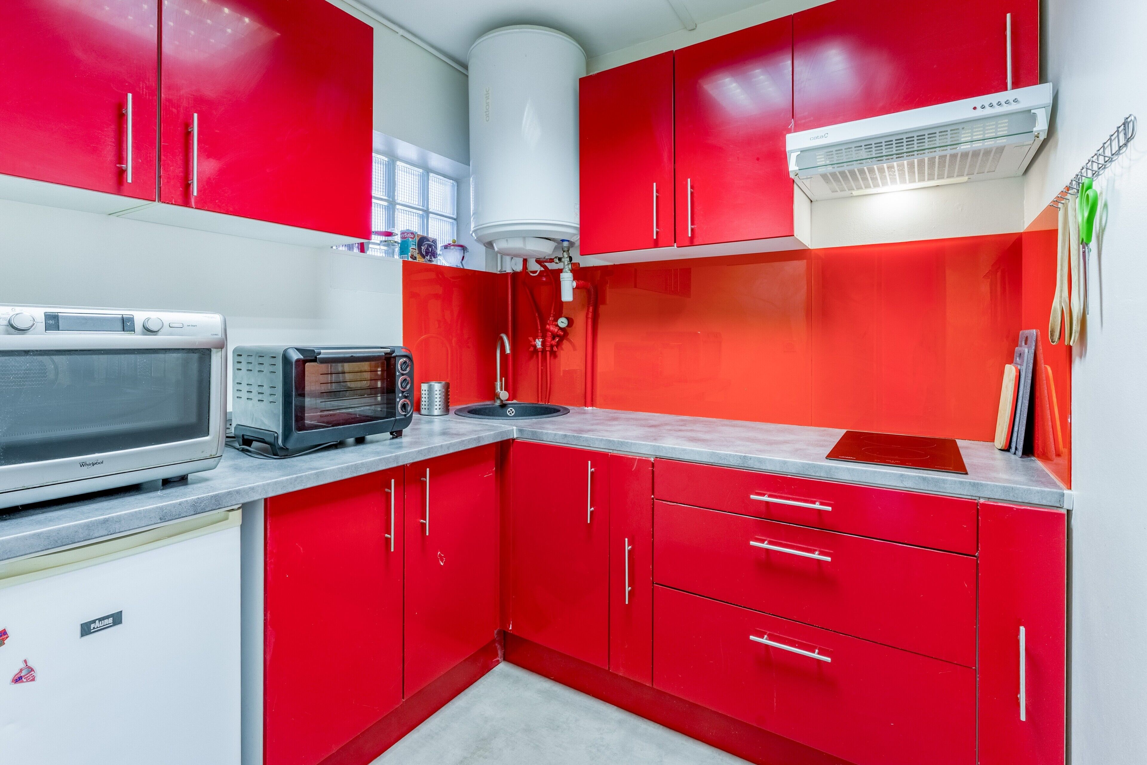 A kitchen with red cabinets, a microwave, a toaster, and a water heater.