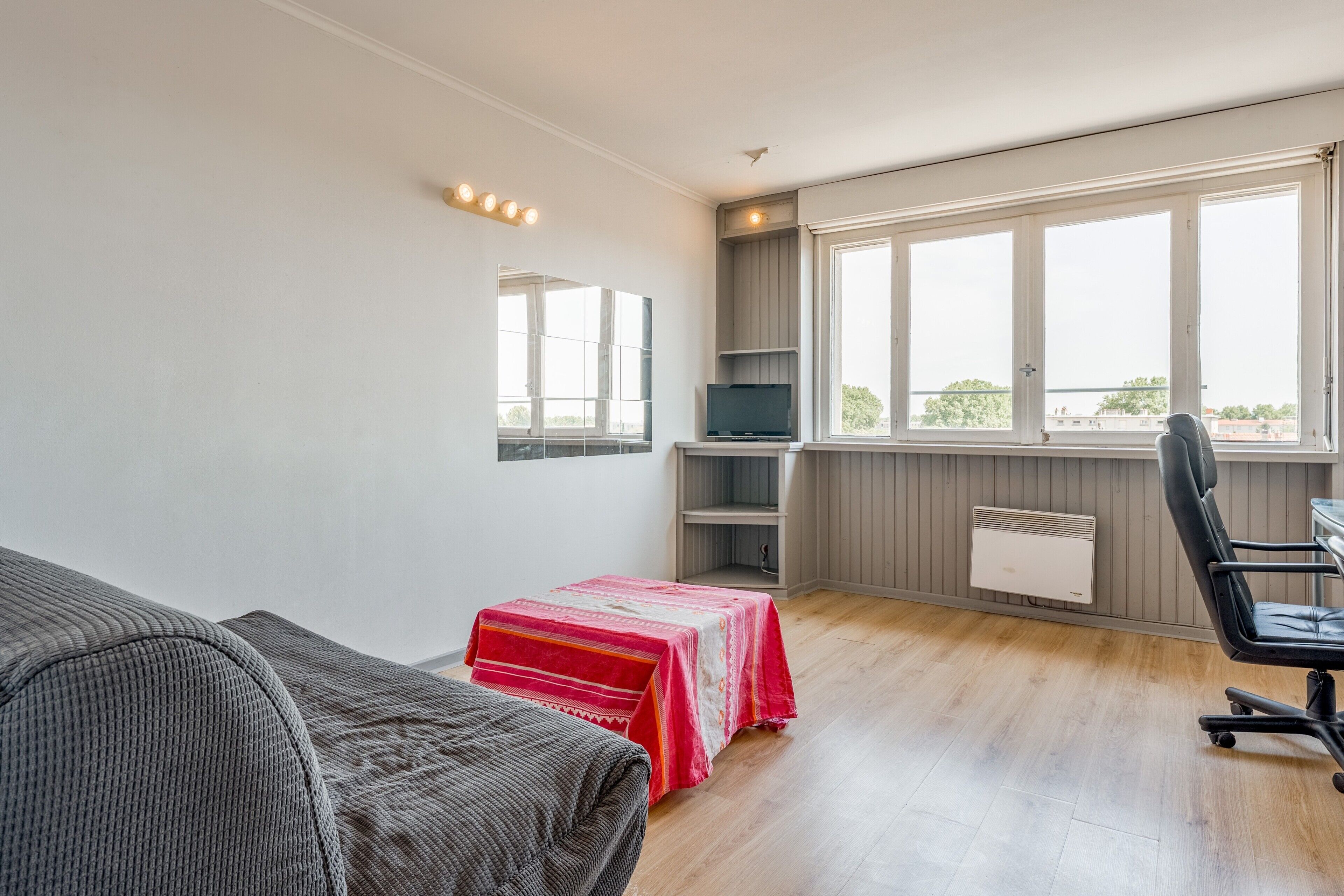 A room with a bed, a desk, a chair, a TV, and a window with a view.
