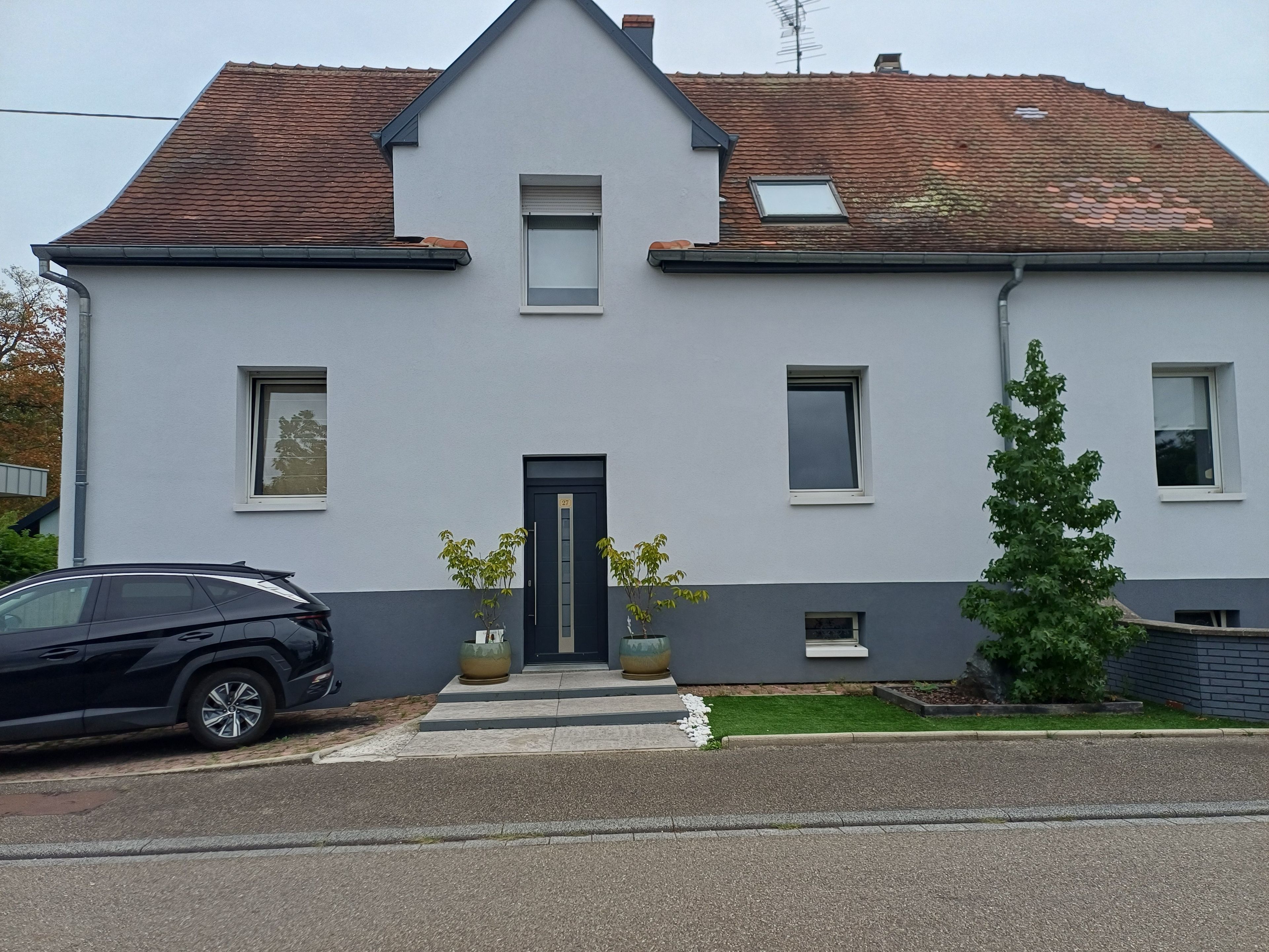 A two-story house with a dark front door, a small porch, and a car parked in front.