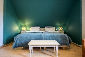 Een slaapkamer met een bed, twee nachtkastjes, een bankje en een groene wand.
