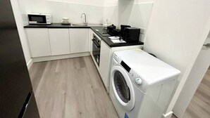 Cozinha compacta com armários brancos, micro-ondas, cafeteira e máquina de lavar.