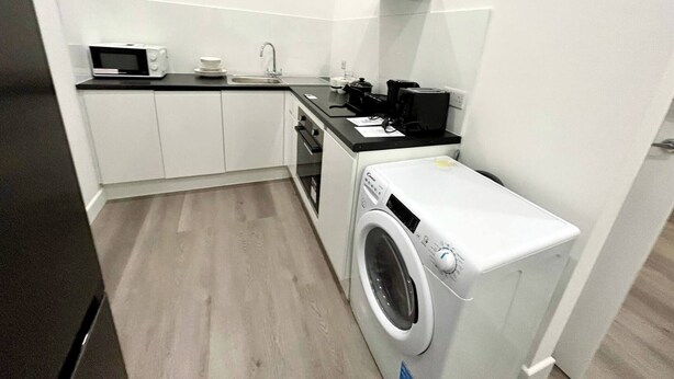 A compact kitchen with white cabinets, a microwave, a coffee maker, and a washing machine. - Beautiful Place to Stay (London)