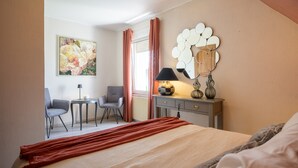 Quarto de hotel com cama, escrivaninha, cadeira, luminária, vaso e um quadro na parede.