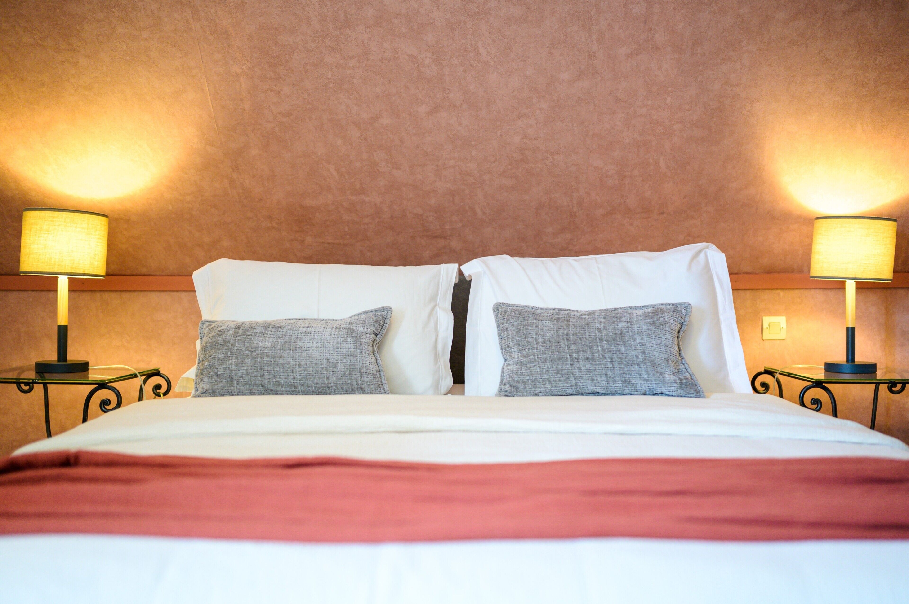 A hotel room with a bed, two bedside lamps, and a textured wall.