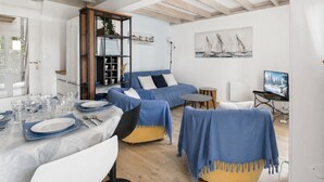 Una sala de estar moderna con comedor, un sofá azul, una estantería de madera y un cuadro en la pared.