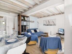 Ein modernes Wohnzimmer mit Essbereich, einem blauen Sofasatz, einem Holzregal und einem Gemälde an der Wand.