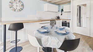 Una cocina moderna con comedor, que incluye un reloj, armarios blancos y techo de madera.