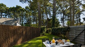 Un área de comedor al aire libre con una mesa dispuesta para dos personas, rodeada por una terraza de madera y un seto.