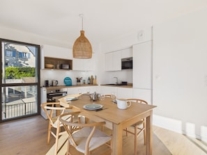 A modern kitchen with wooden cabinetry, a dining table with chairs, and a hanging light fixture. - Apartment for 4, terrace, 200 m from the port (Pléneuf-Val-André)