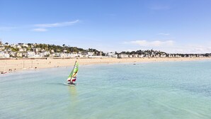 Ein Strand mit einem Segelboot, klarem Wasser und einer Küstenstadt im Hintergrund.