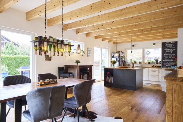 A modern kitchen with wooden beams, a dining area with chairs, and a view of the outdoors.